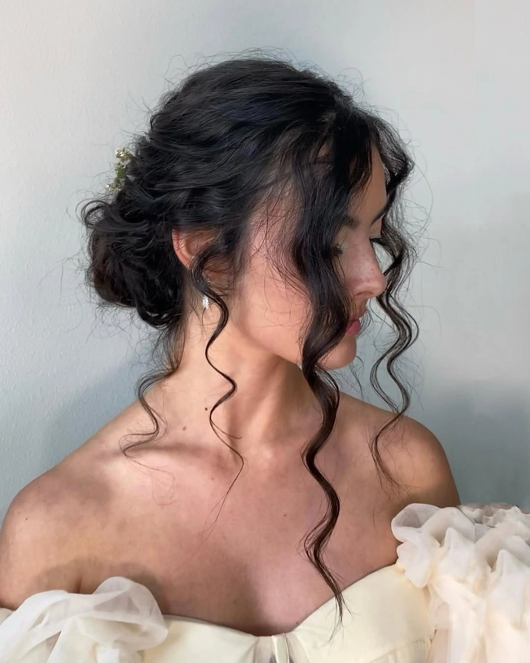 Fall hairstyles for wedding guests 2026 Soft Romantic Low Bun with Natural Curly Tendrils