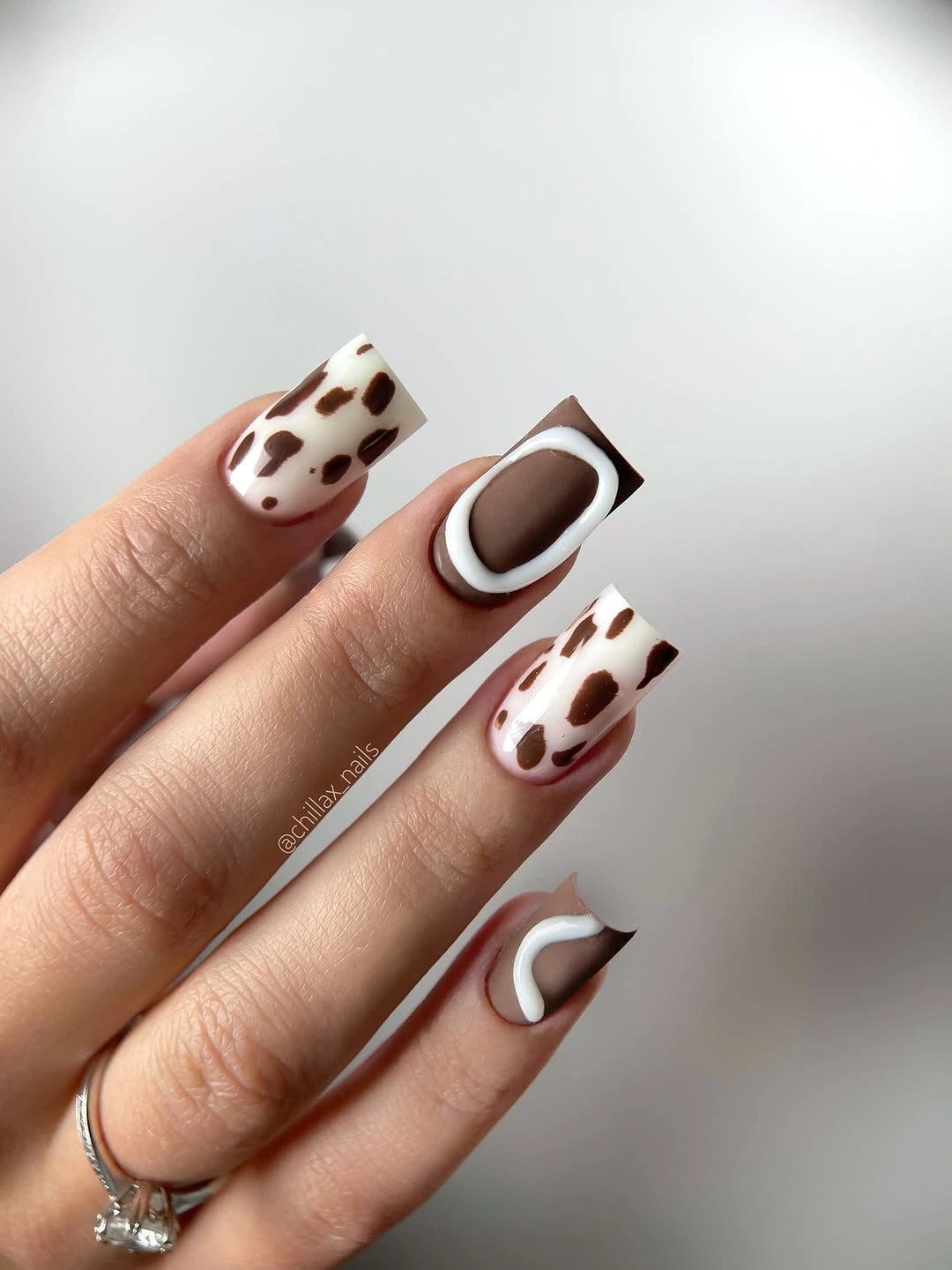 Brown and white cow print almond nails with curved accents