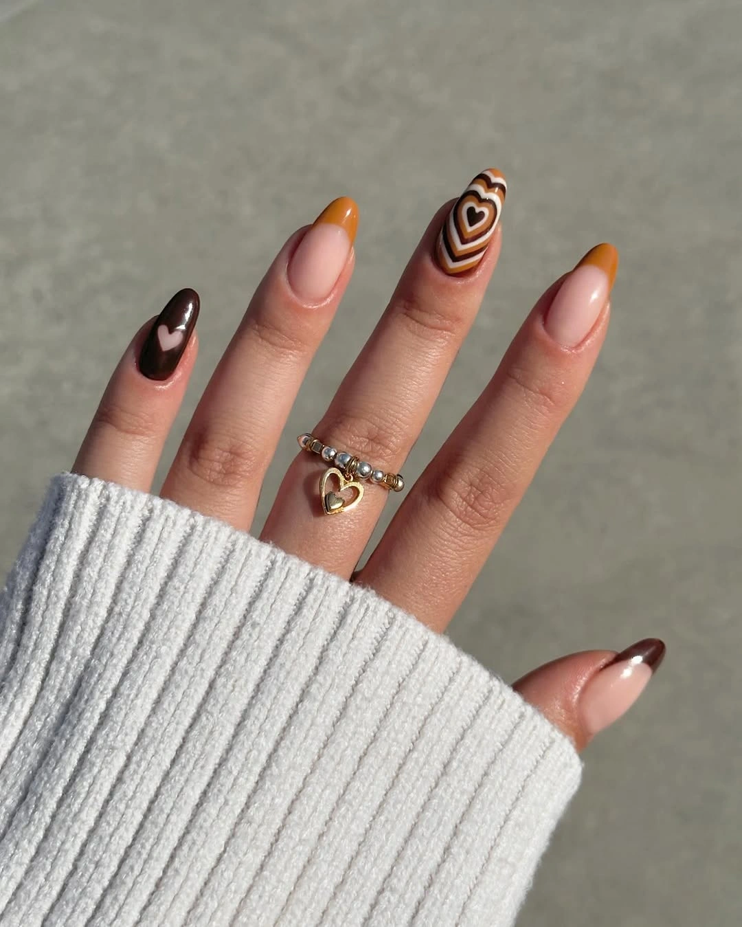 Nude almond nails with brown French tips and tiny heart accents