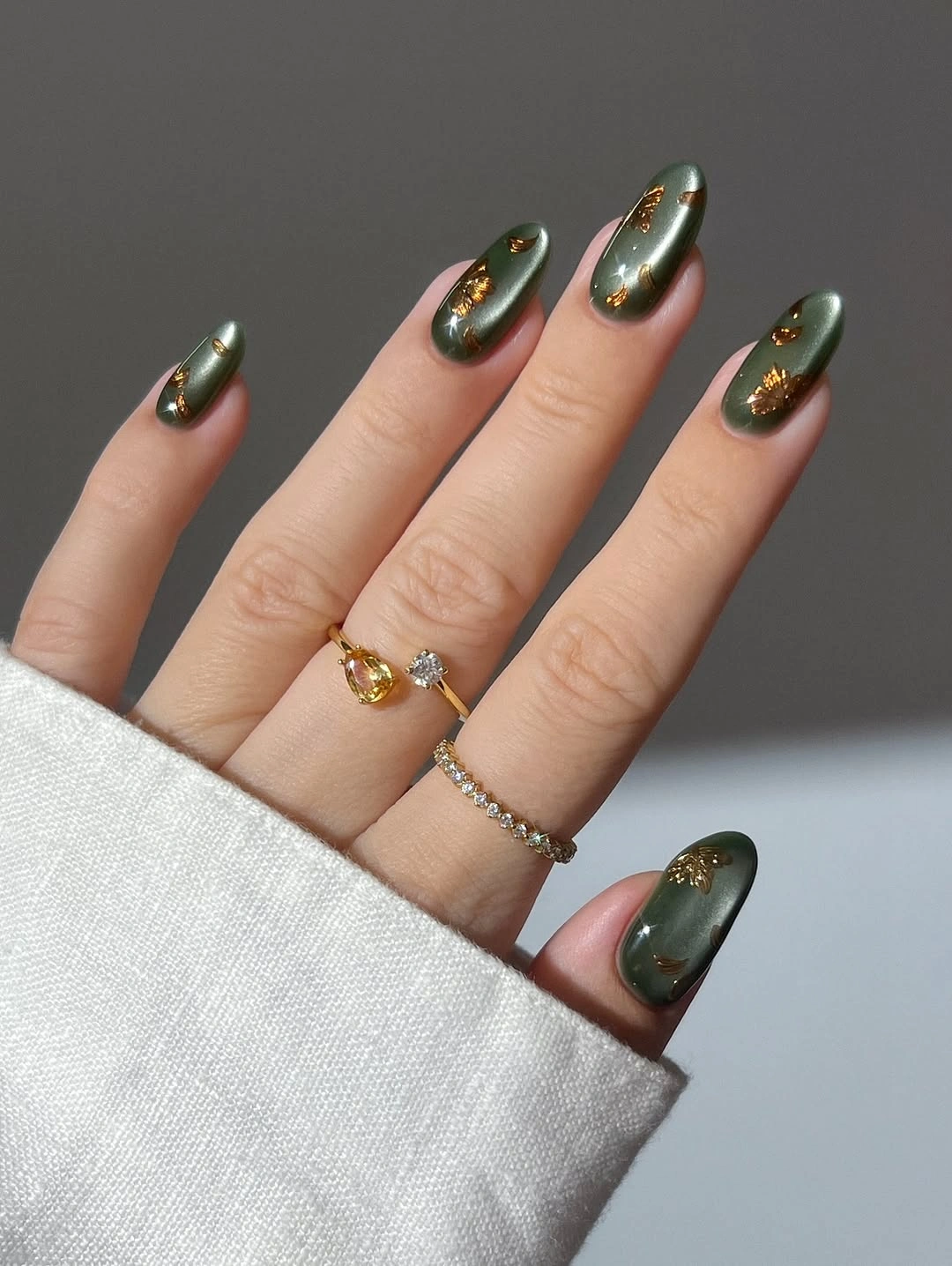Muted green oval nails with small gold accents