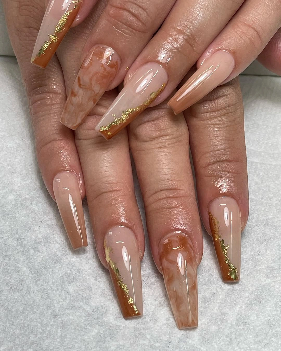Long square nude nails with orange red tips gold edging and floral detail
