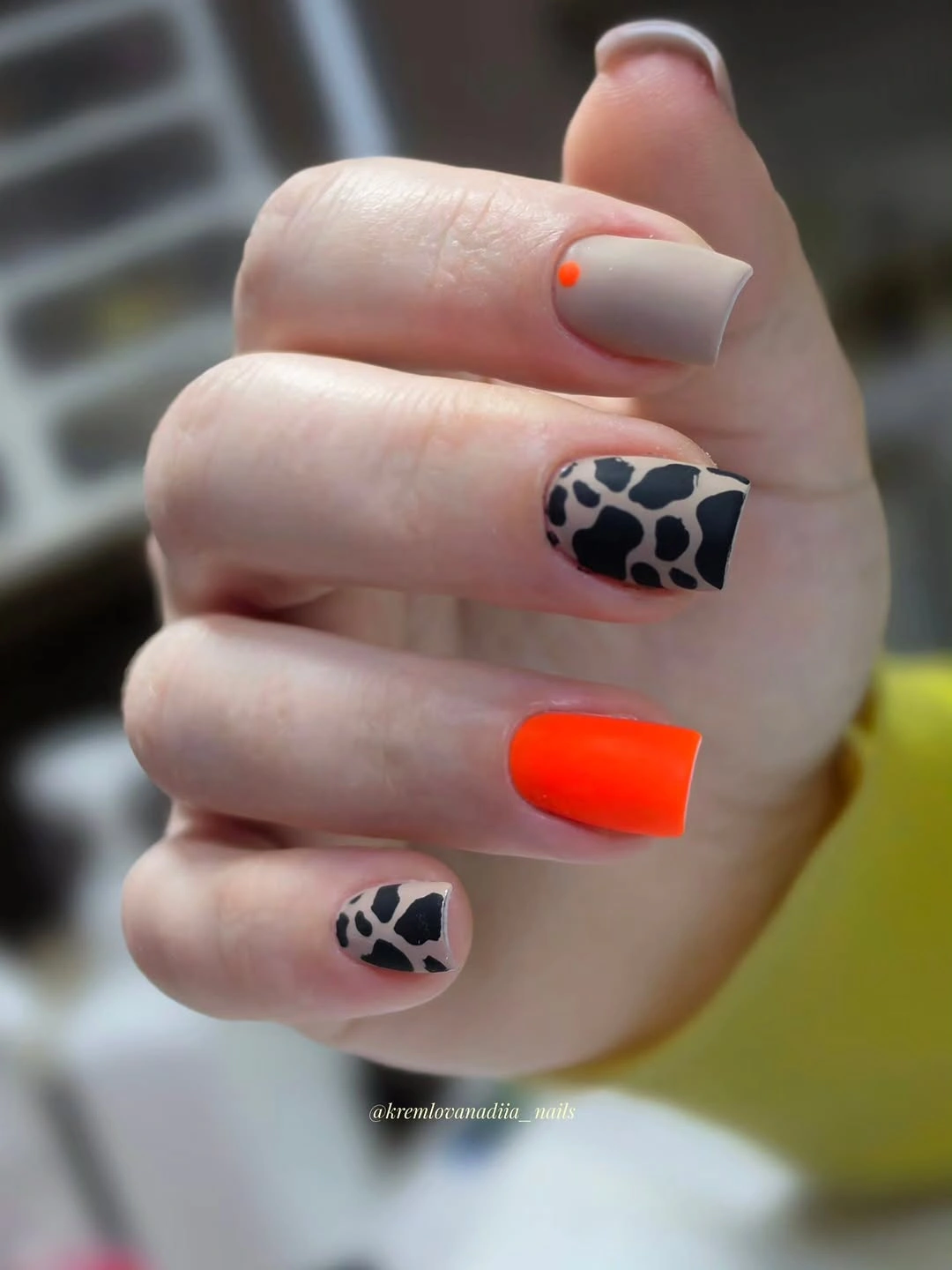 Short taupe nails with a bright orange nail and cow print accent