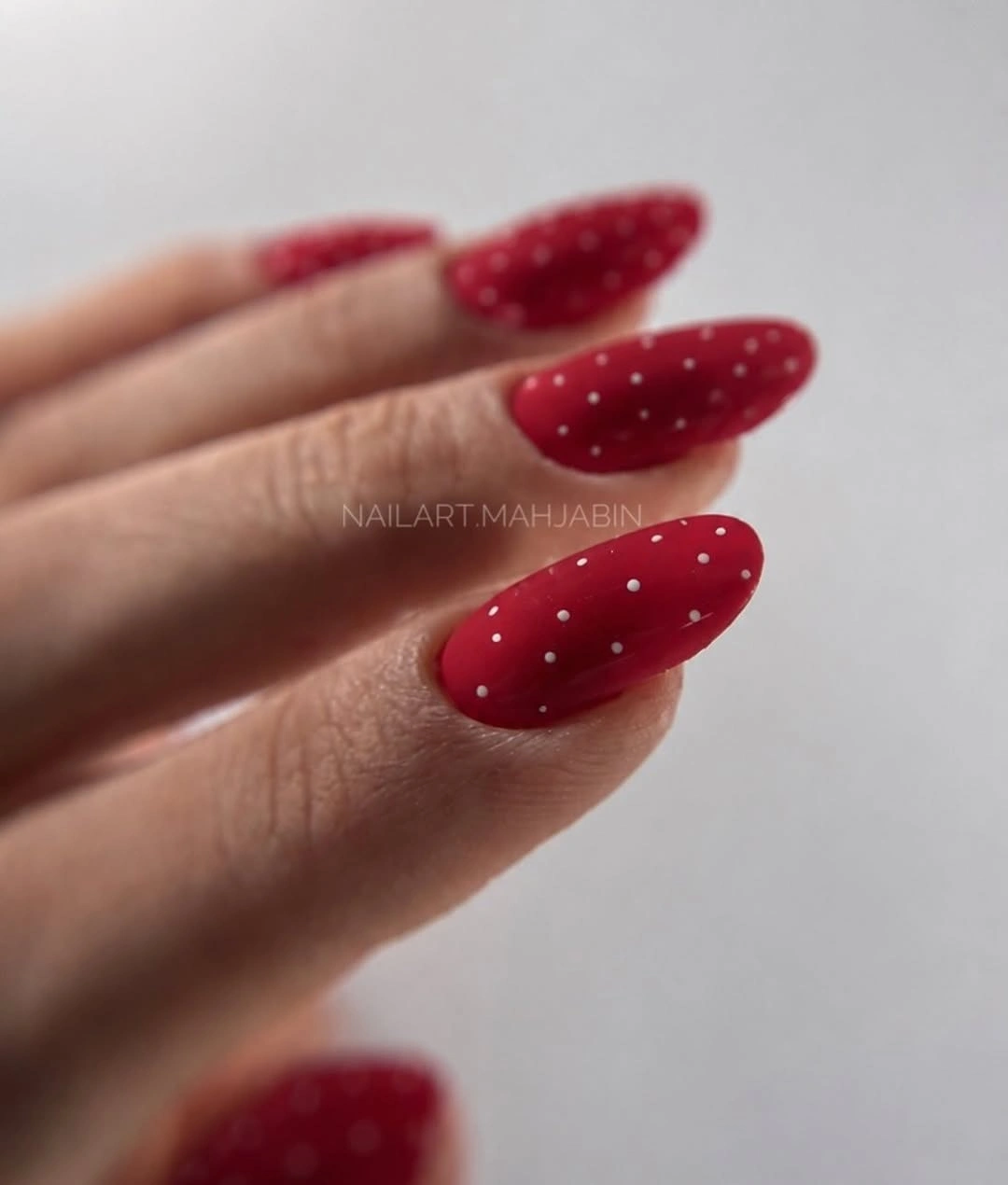 Red almond nails covered with evenly spaced pale dots