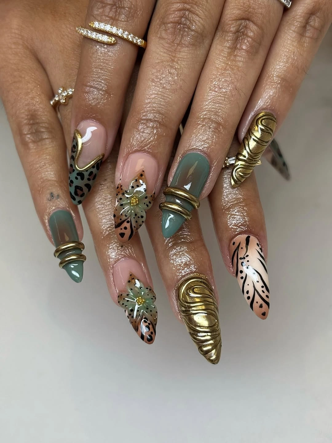 Sage green pointed nails with gold bands and patterns