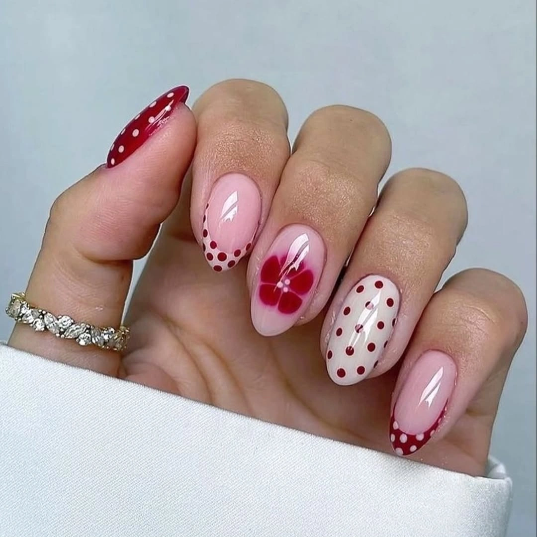 Blush nails with red dotted French tips and flower detail
