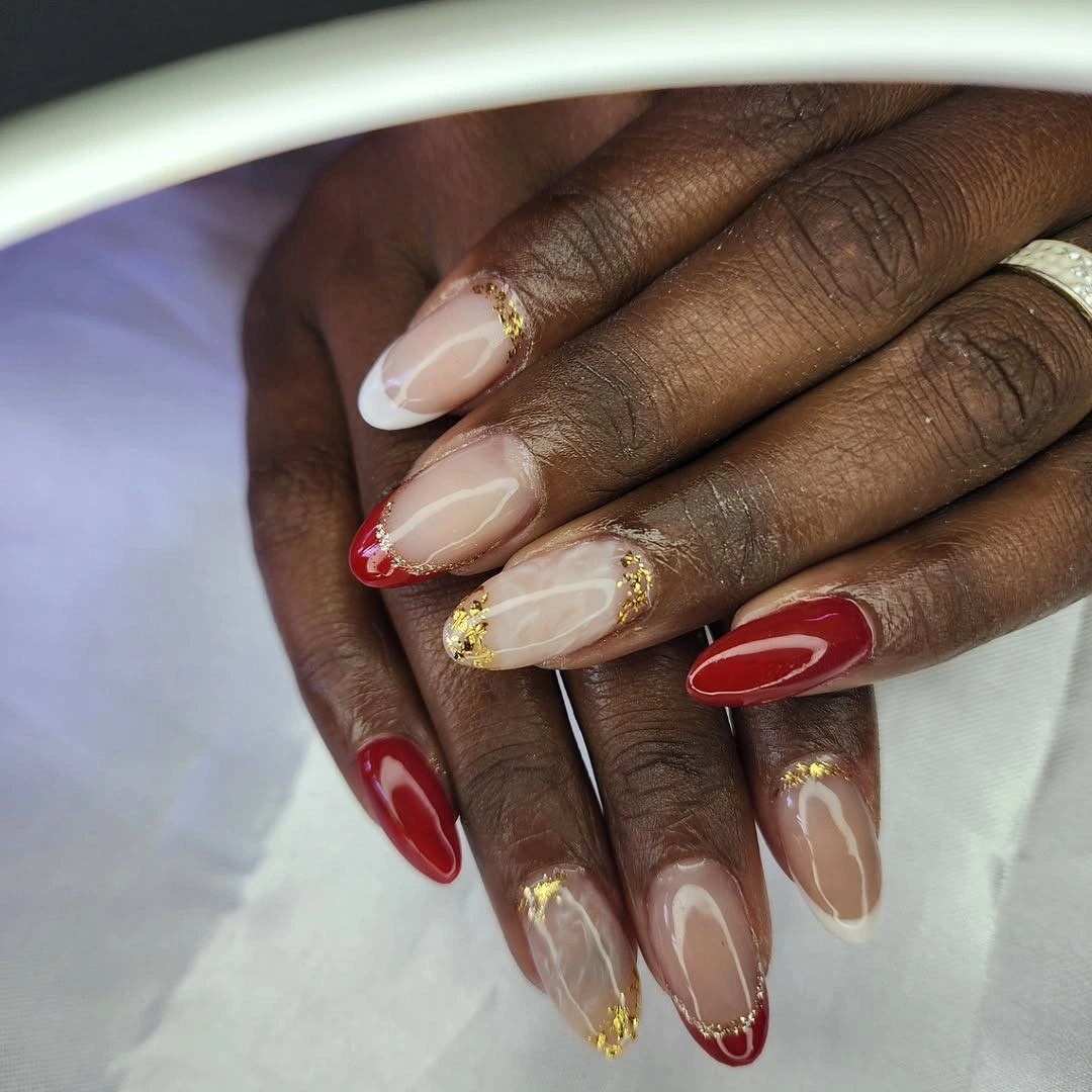 Long stiletto nails with sheer nude sections red tips gold chains and charms