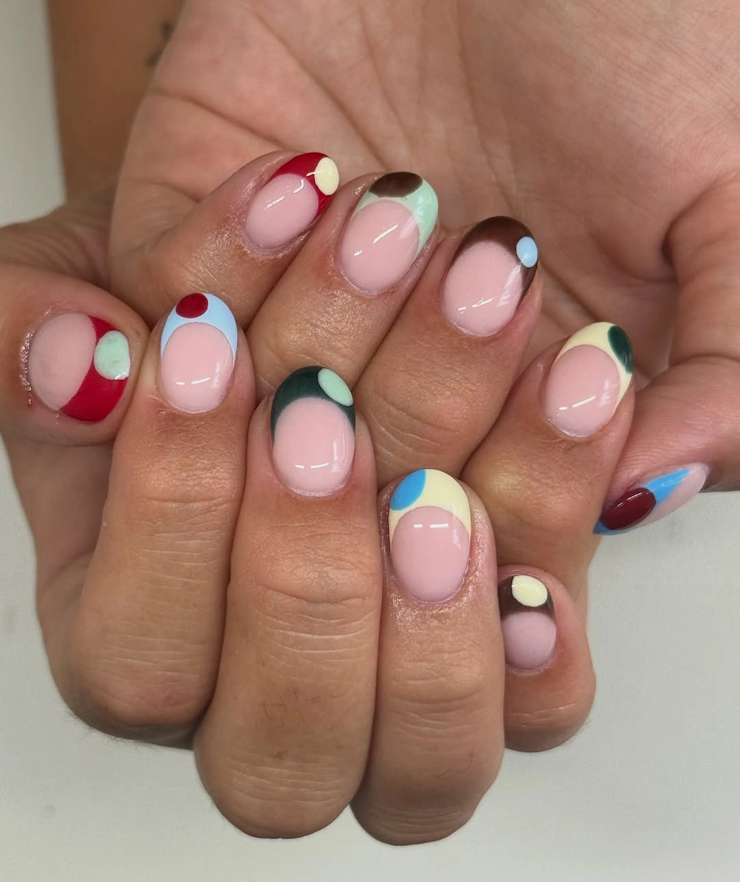 Short clear pink nails with colorful dots and curved tips