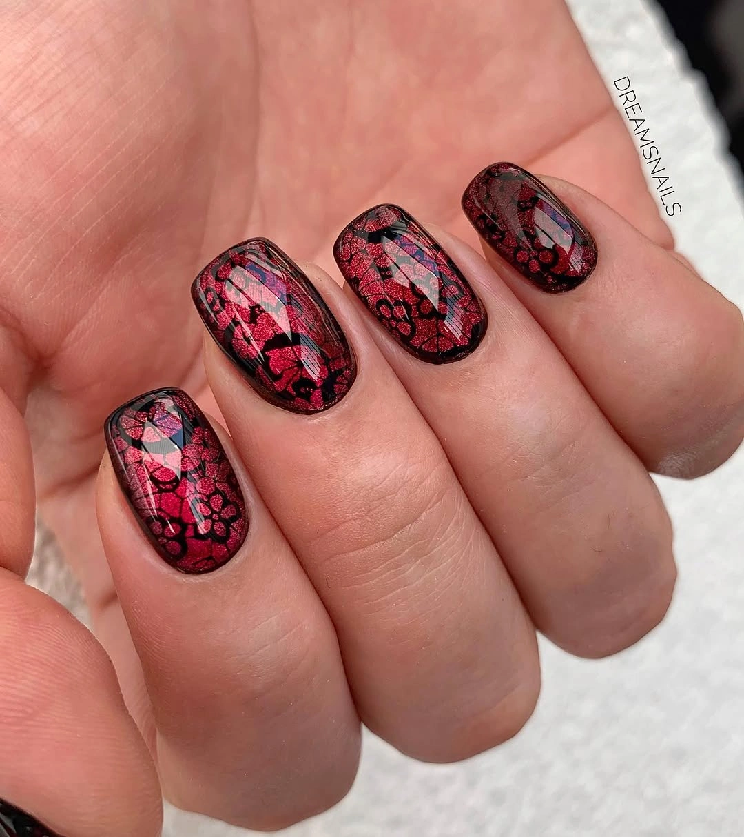 Short berry red square nails with a dark floral lace overlay