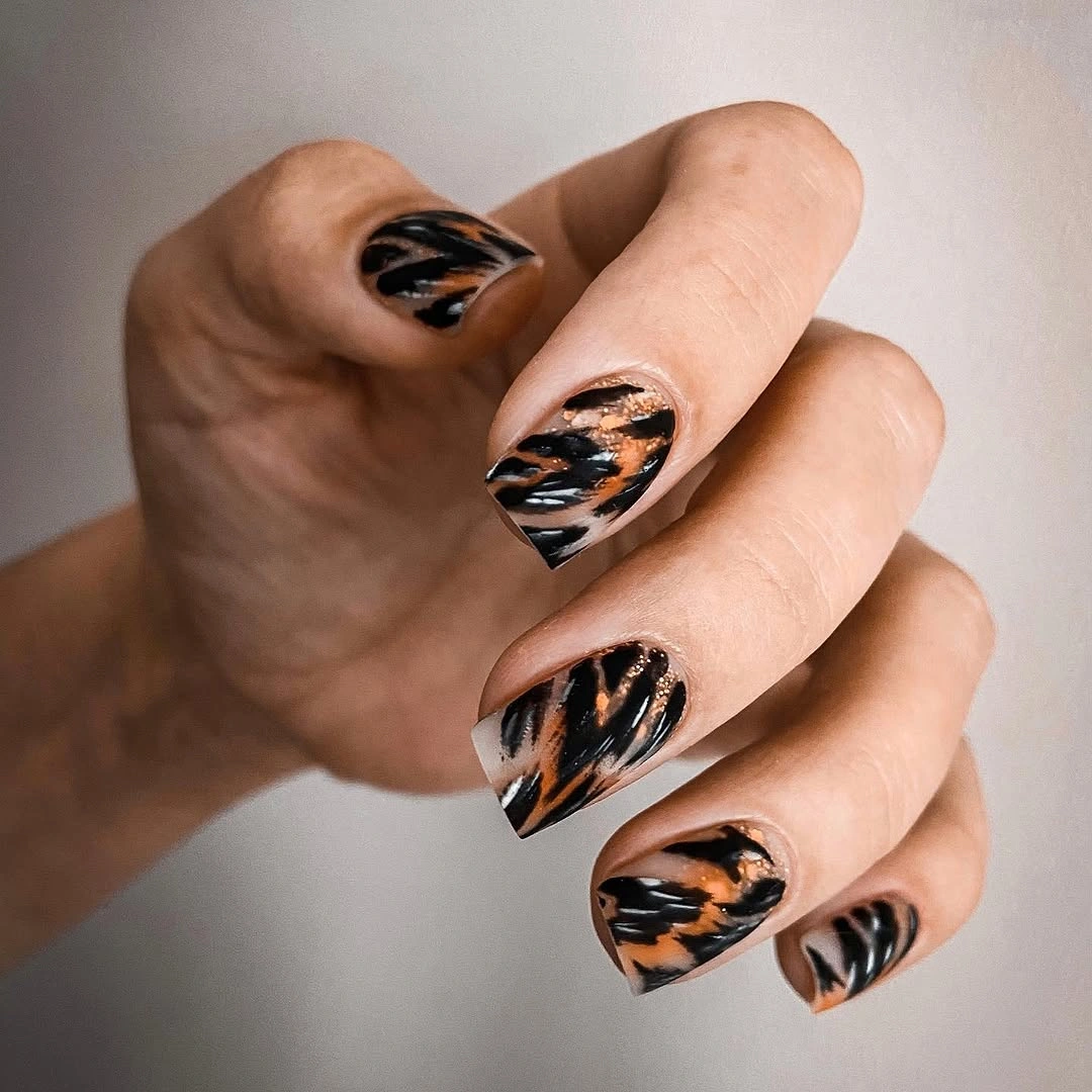 Short peach oval nails with black and orange swirl accents