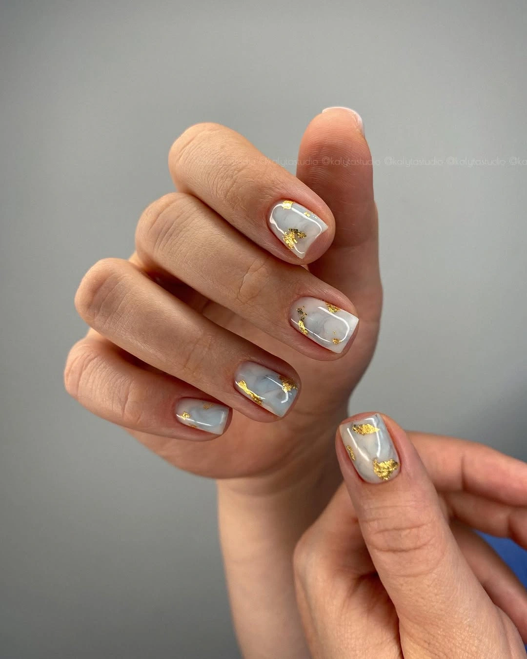 Short pearly gray white nails with irregular gold metallic patches