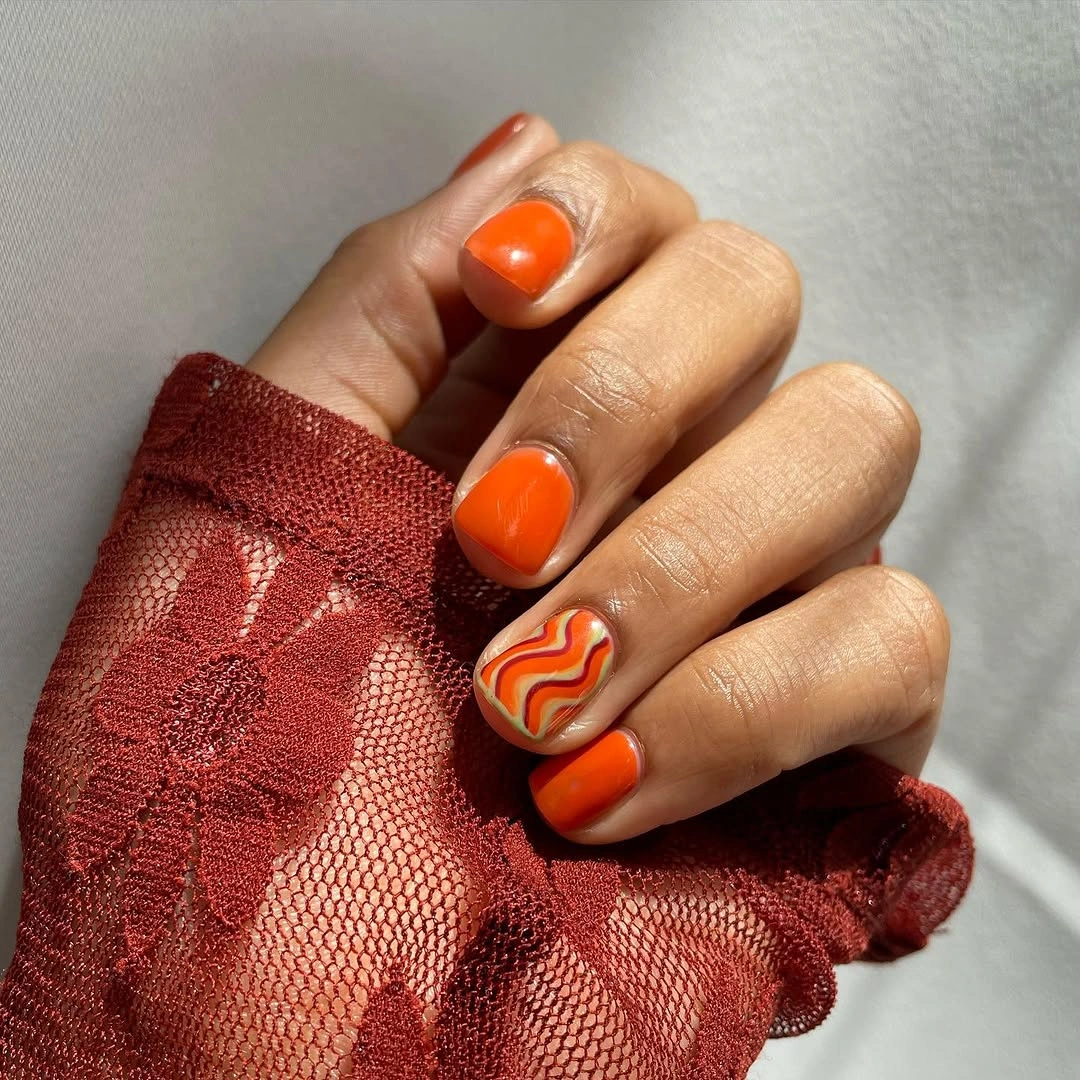 Short orange nails with one coral and pale wavy accent nail