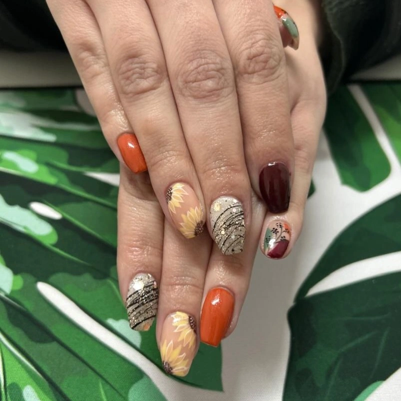 Short orange and burgundy nails with leaf stripe and glitter accents