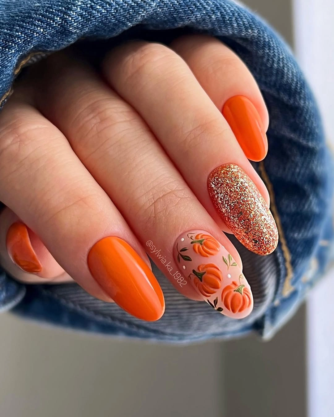 Bright orange almond nails with bronze glitter and small autumn accents