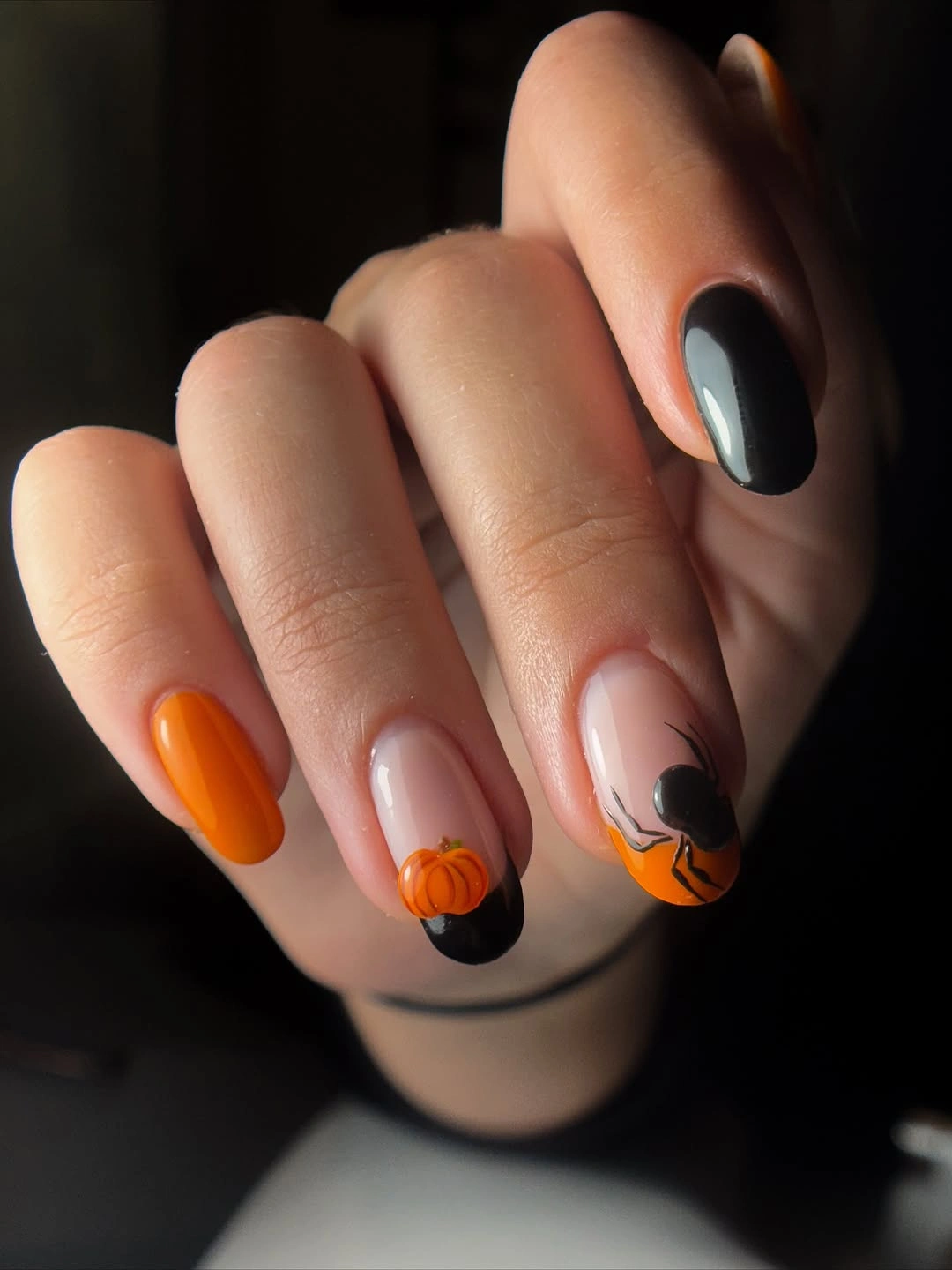 Short rounded nude nails with orange tips and dark seasonal accents