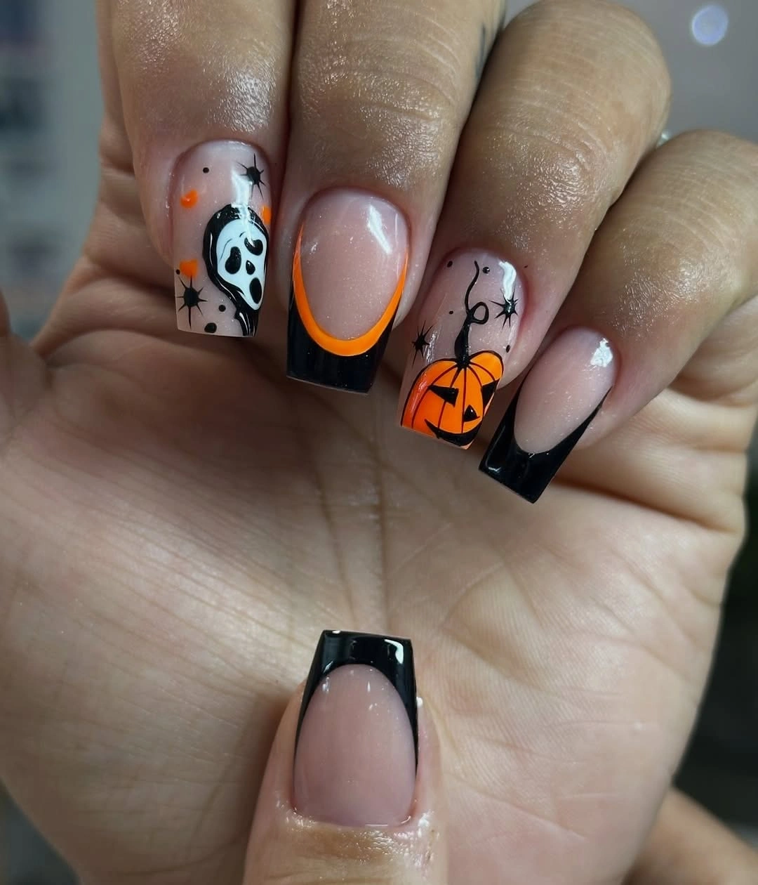 Short square nude nails with dark borders and orange pumpkin accents
