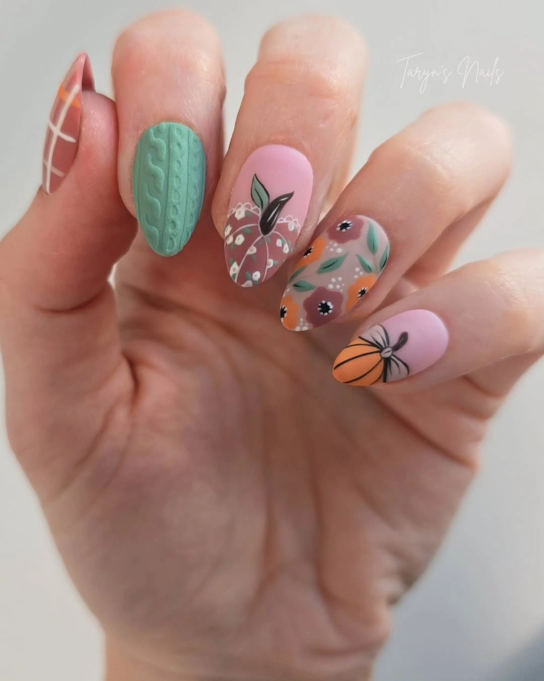 Pastel pink nails with a textured green accent and small fall motifs