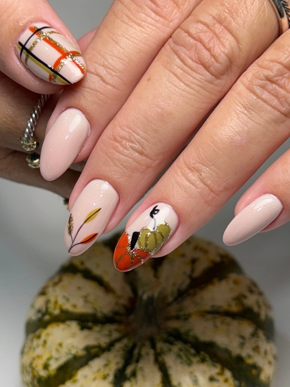 Pale pink almond nails with fine plaid lines and one orange pumpkin accent