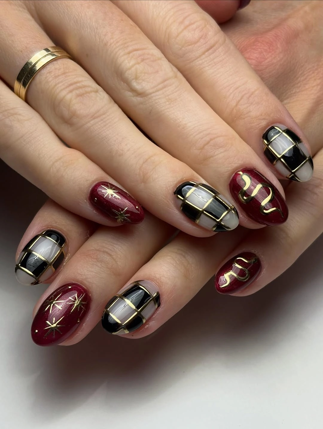 Short almond burgundy nails with black and gold plaid panels