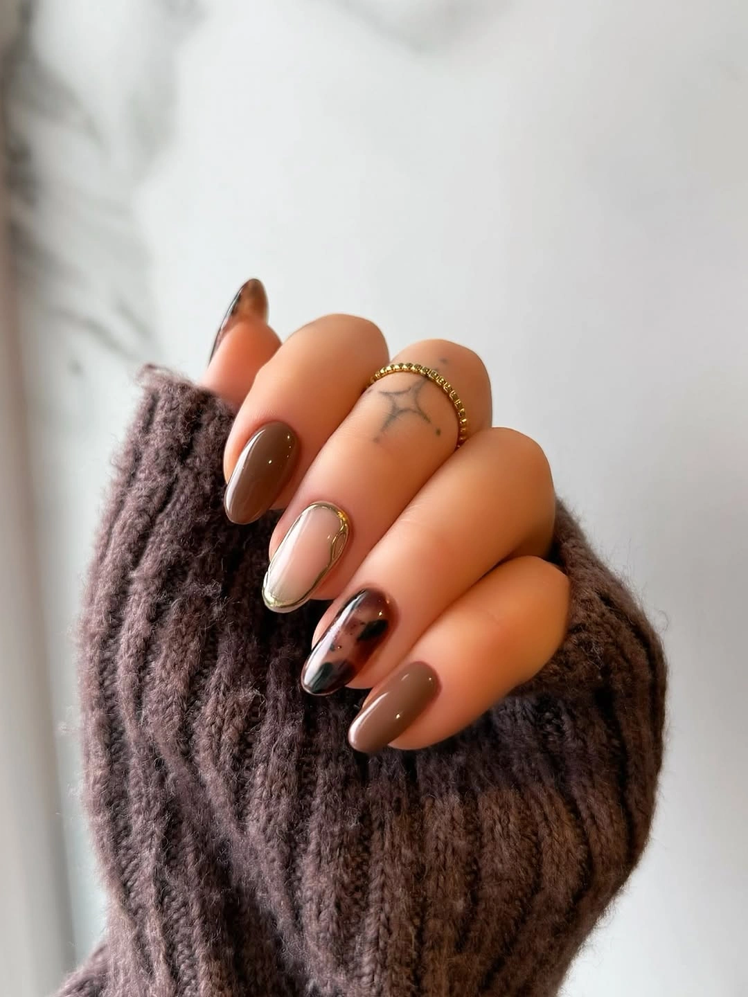 Short almond nails in warm brown and nude with one dark accent