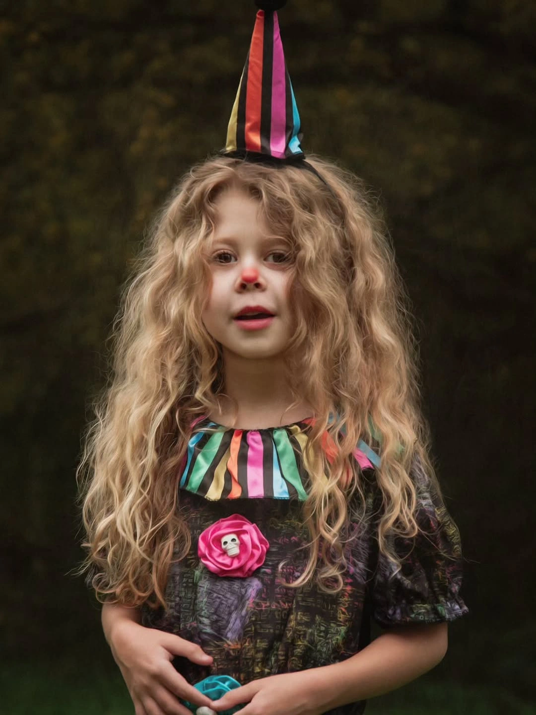 Child in striped witch Halloween costume with tall pointed hat multicolor collar dark dress and pink flower