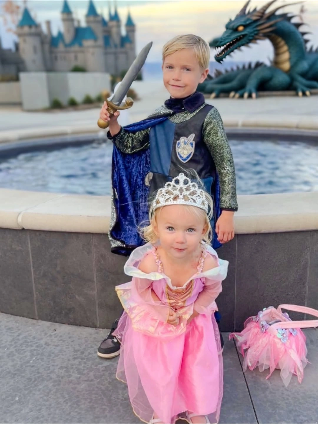 Children in storybook prince and princess costumes with blue silver cape toy sword pink gown and tiara