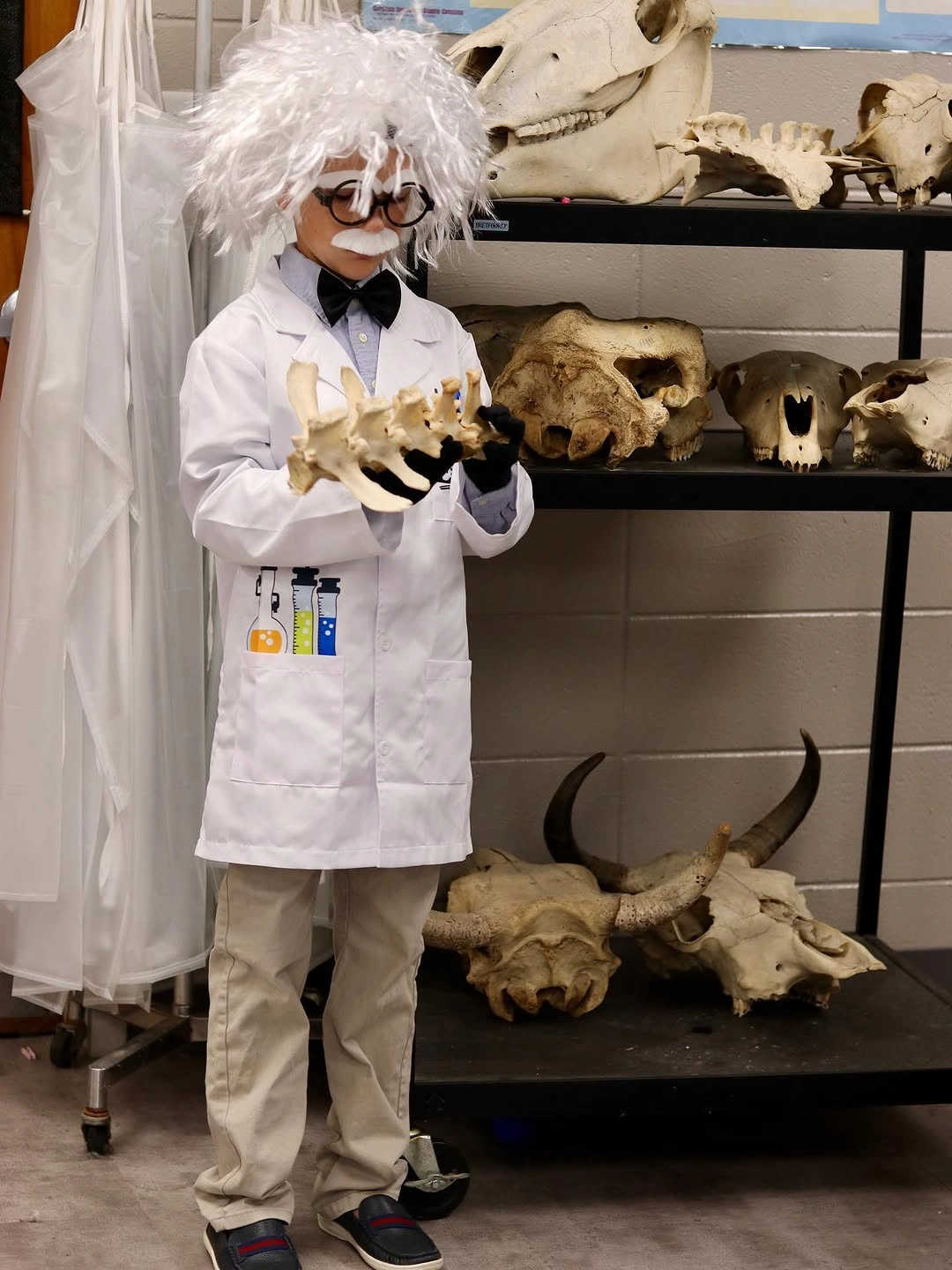Child dressed as Albert Einstein with white lab coat wild white wig round black glasses bow tie gloves and science props