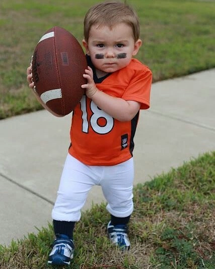 Child in orange football player costume with numbered jersey white trousers athletic shoes eye paint and football