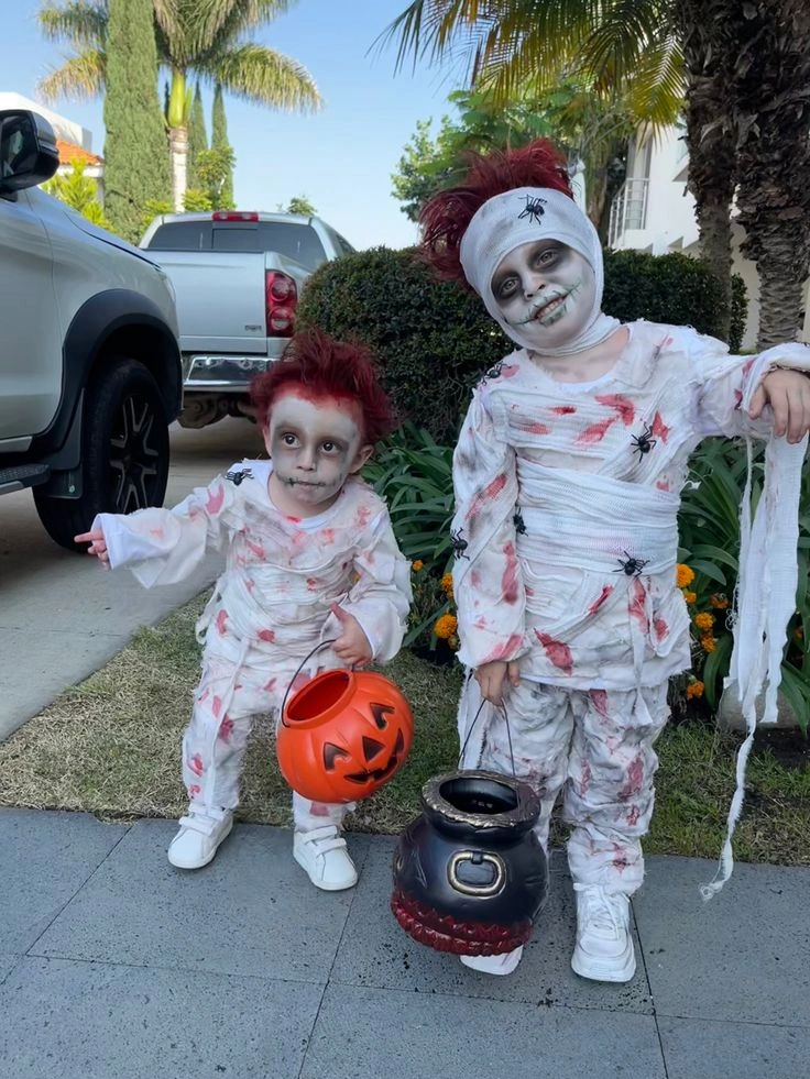 Family group in coordinated mummy Halloween costumes with white wraps red stain effects and pumpkin bucket