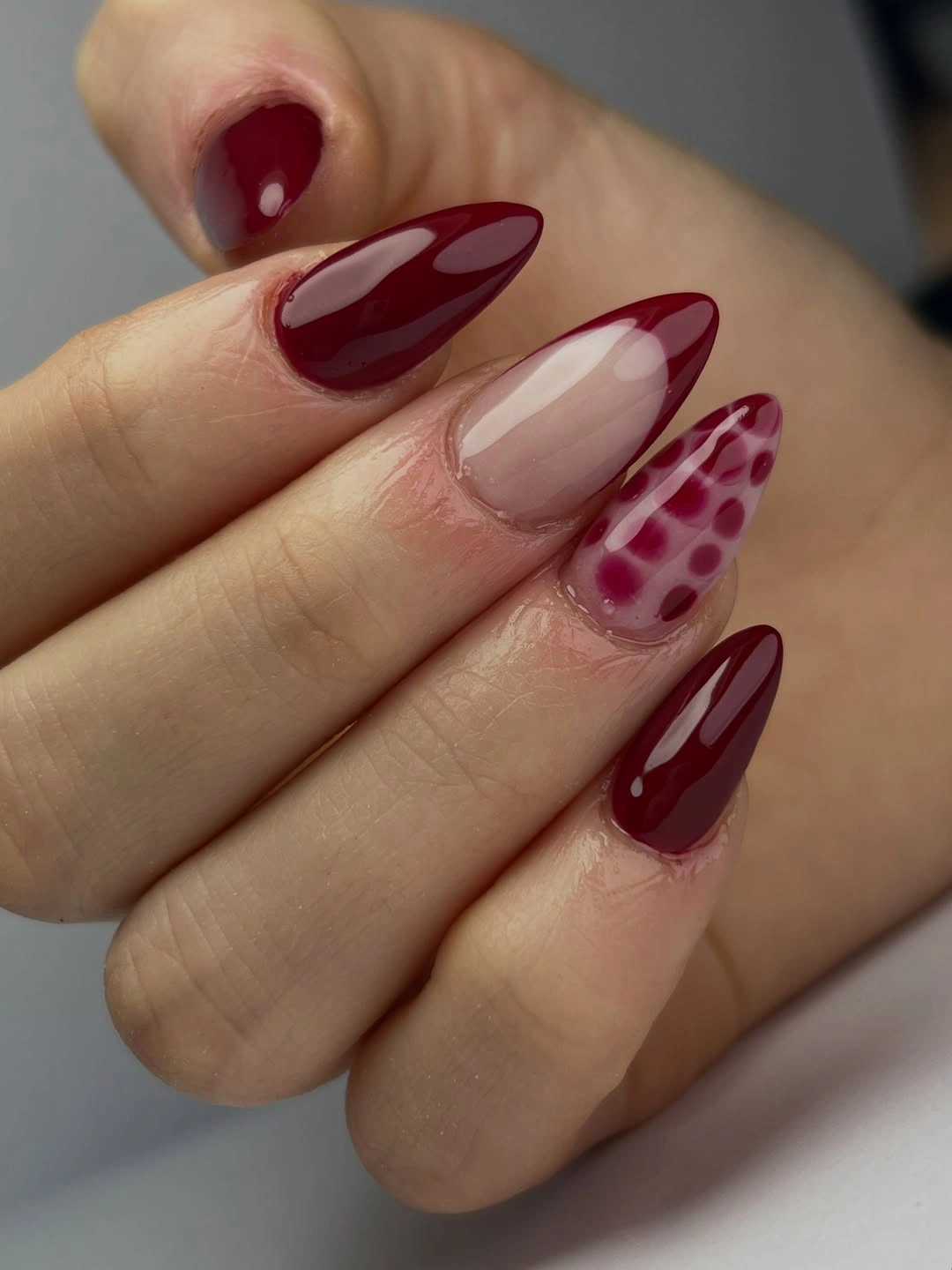 Burgundy almond nails with nude curved panels and spotted accent nail