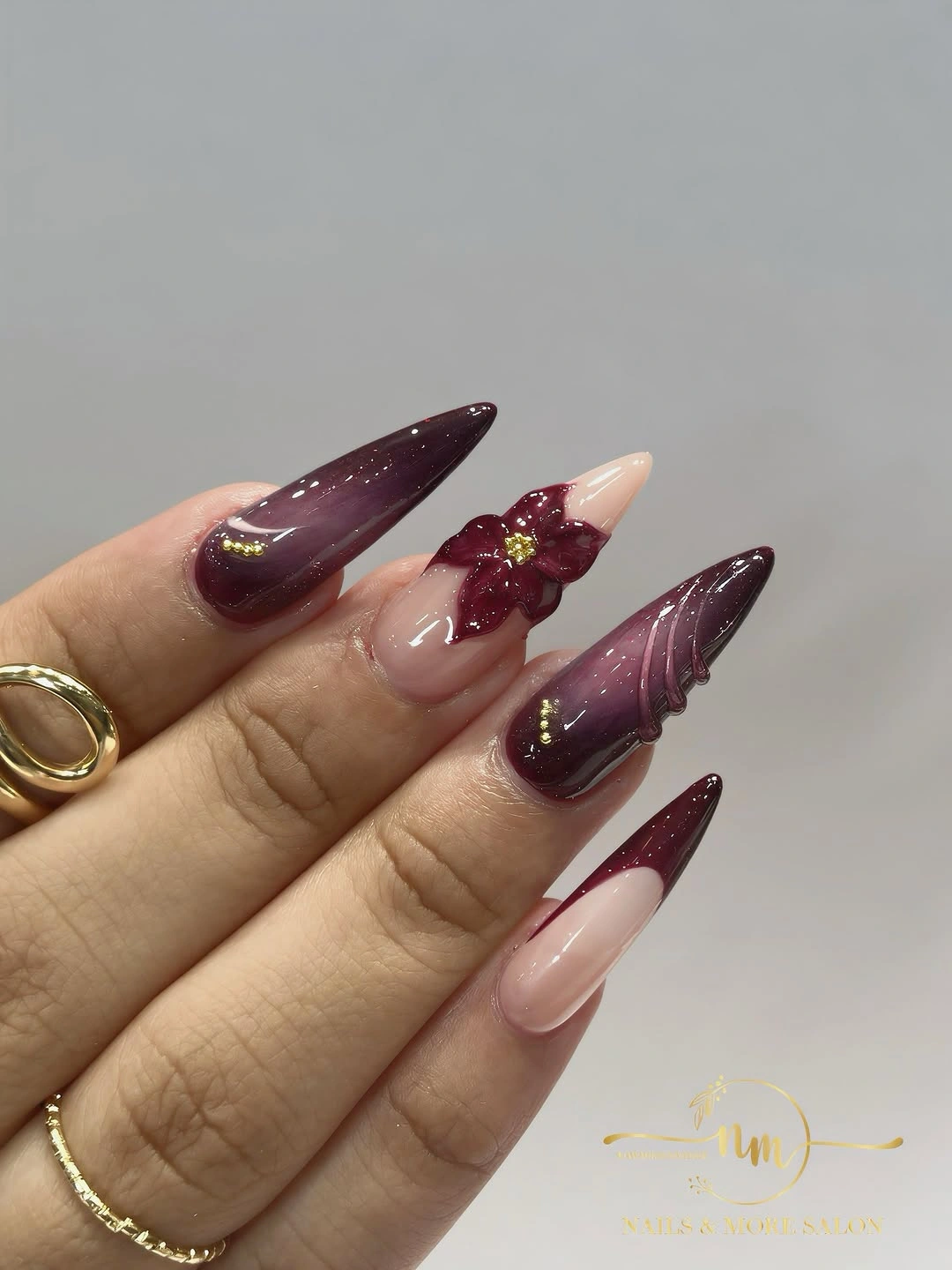 Long plum stiletto nails with nude panels and gold colored accents