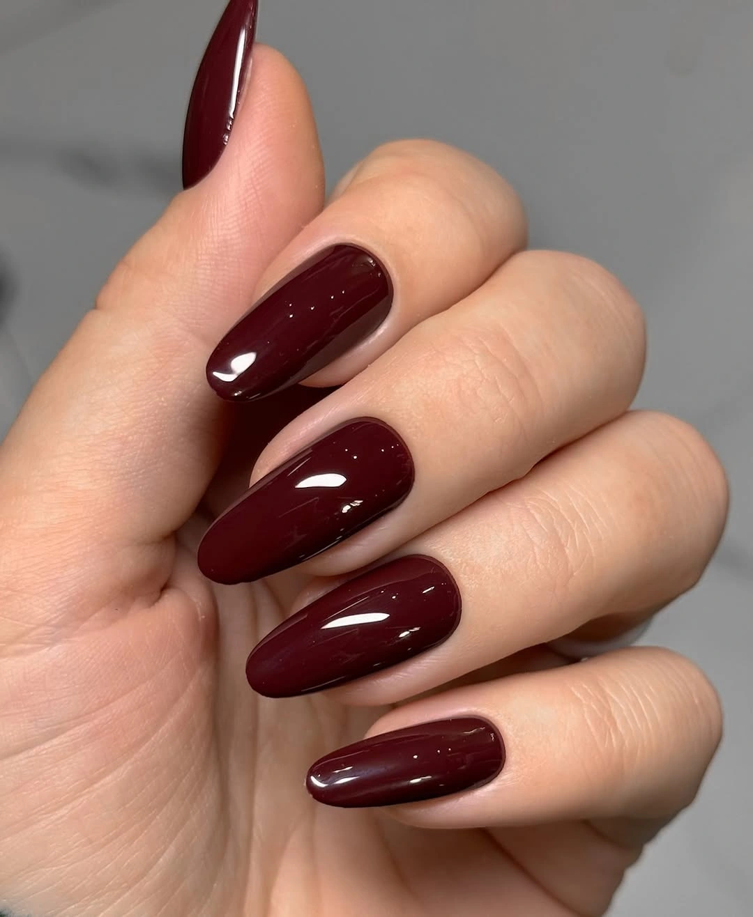 Glossy medium almond nails in a deep solid burgundy color