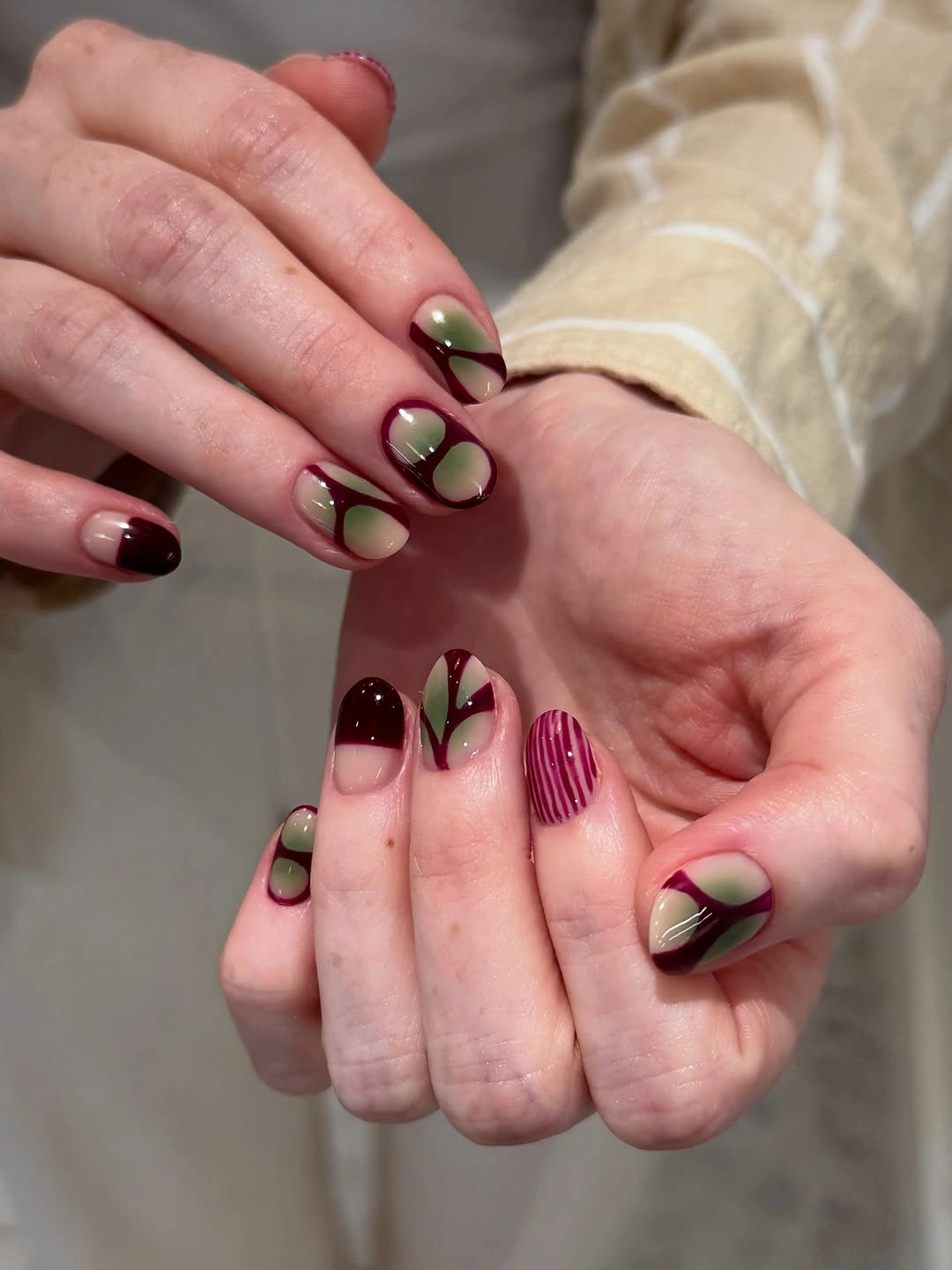 Square olive green and maroon nails with abstract dark graphic patterns