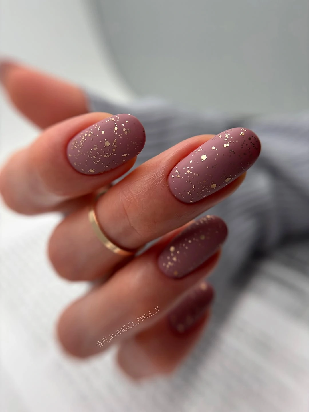 Muted mauve oval nails with sparse small gold colored flecks
