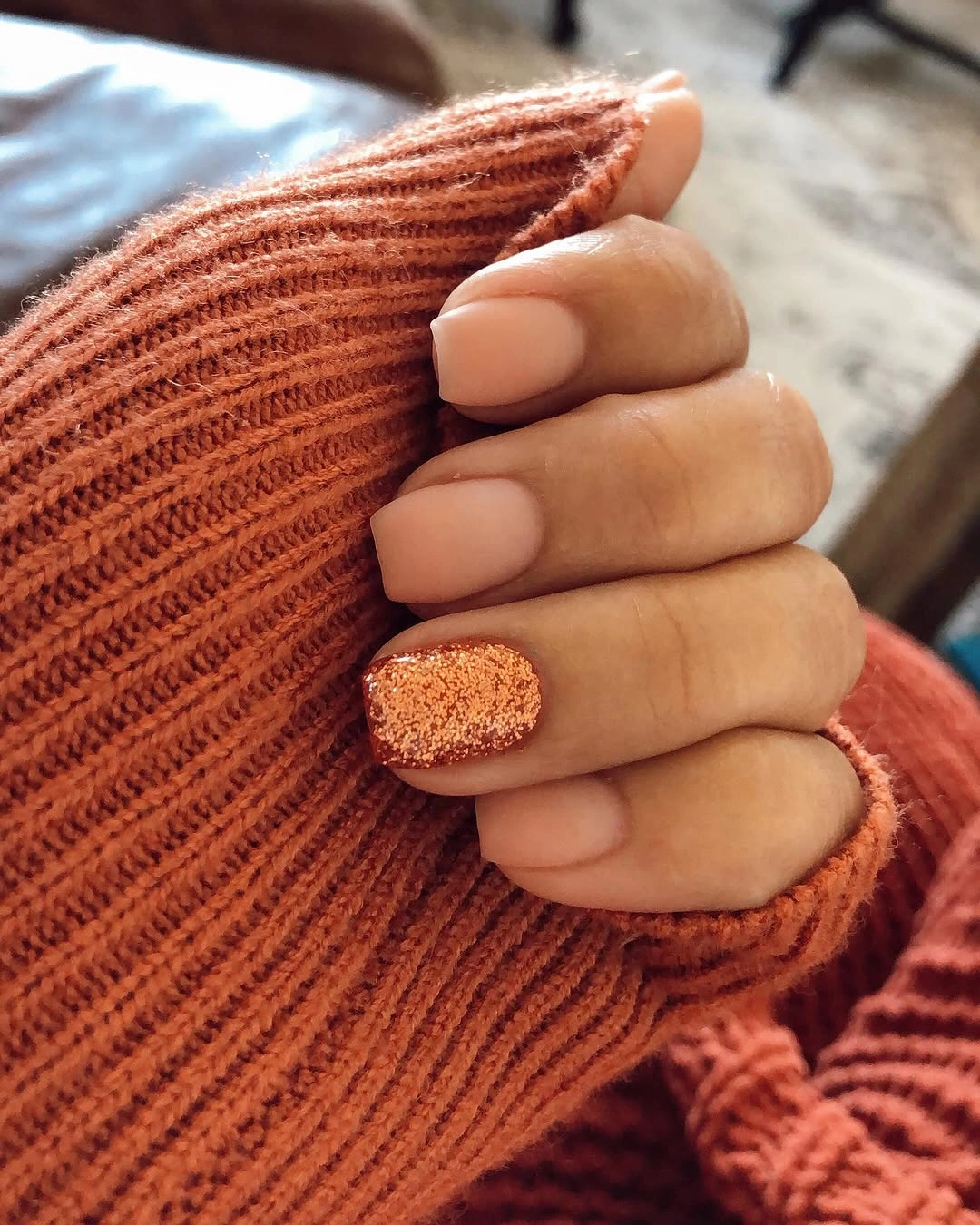 Short nude nails with one bright orange textured looking accent nail