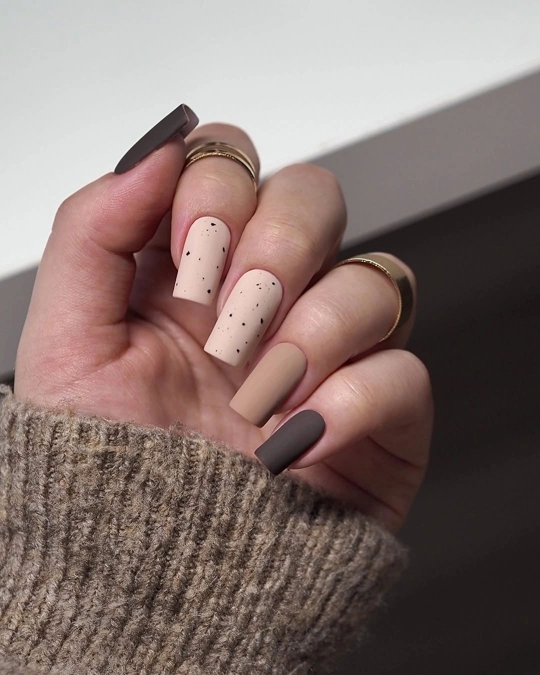 Beige square nails with fine dark speckles and asymmetrical brown accents