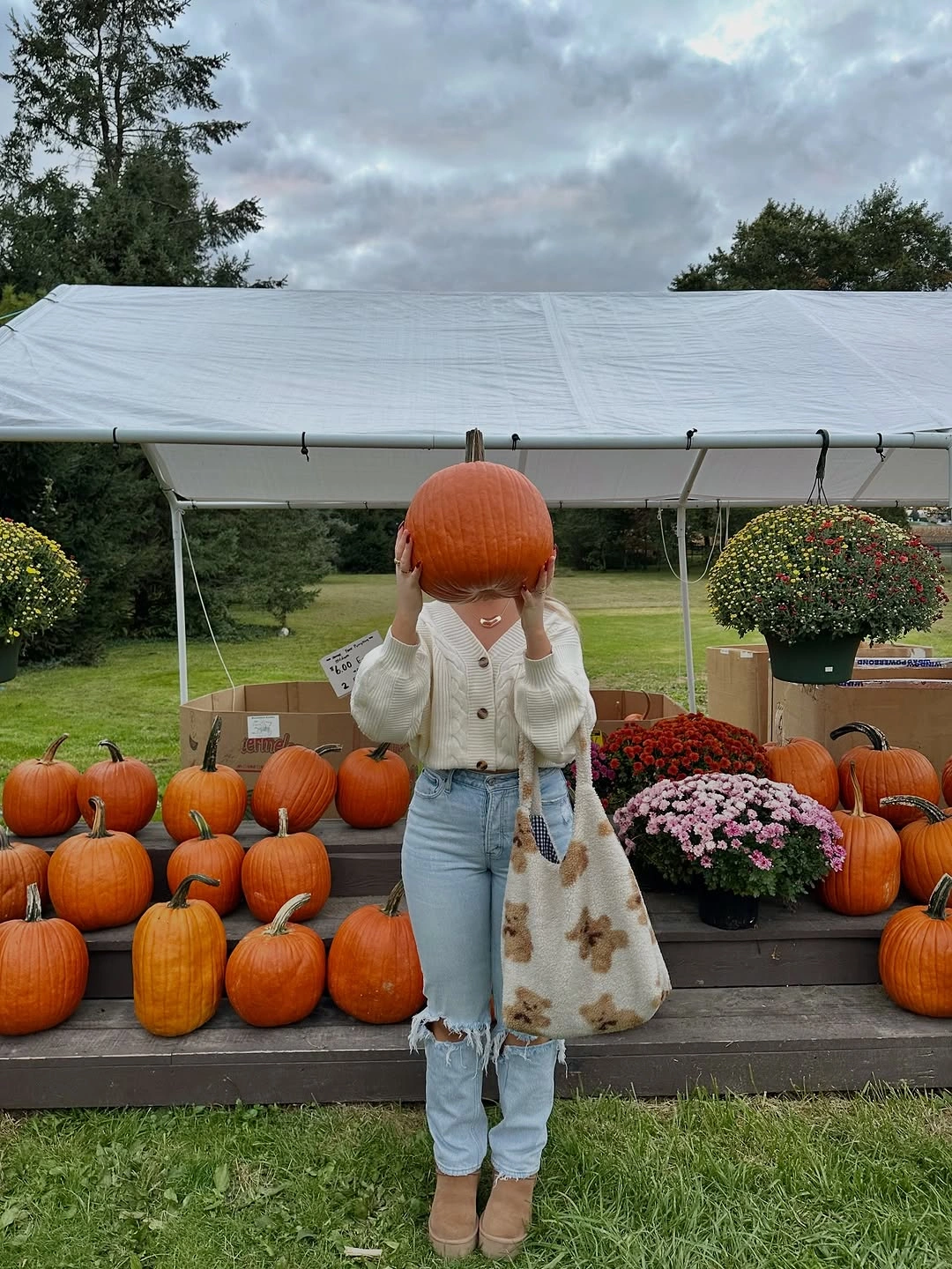 Orange knit hat with pale textured top, light blue jeans, and cream floral tote