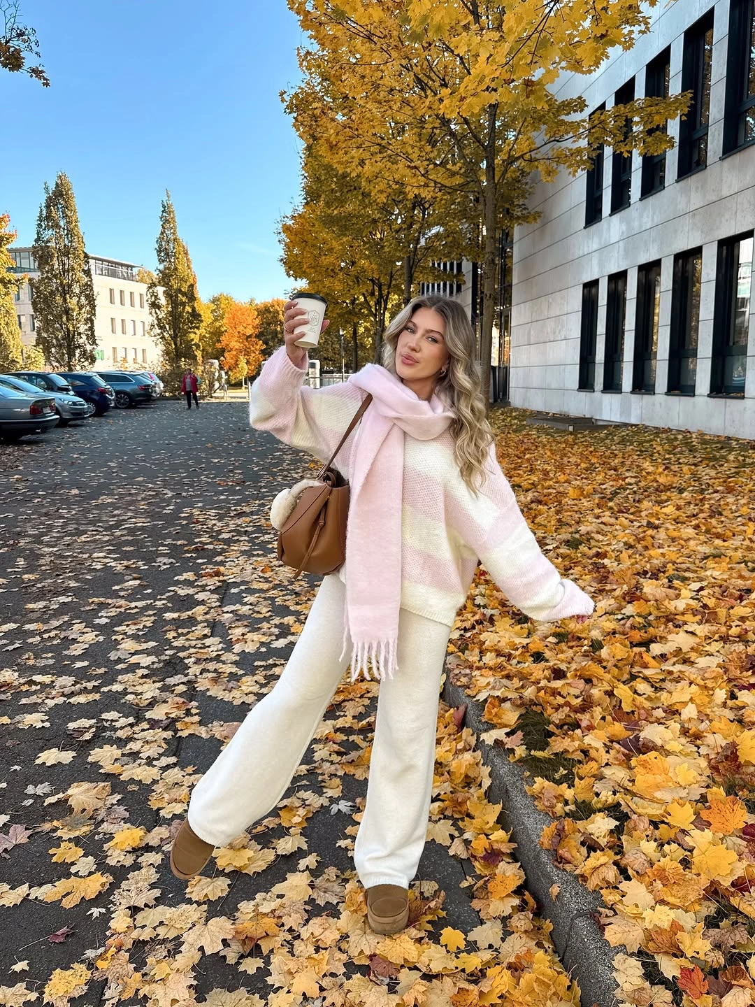 White sweater and wide white trousers with long pale pink scarf and tan bag