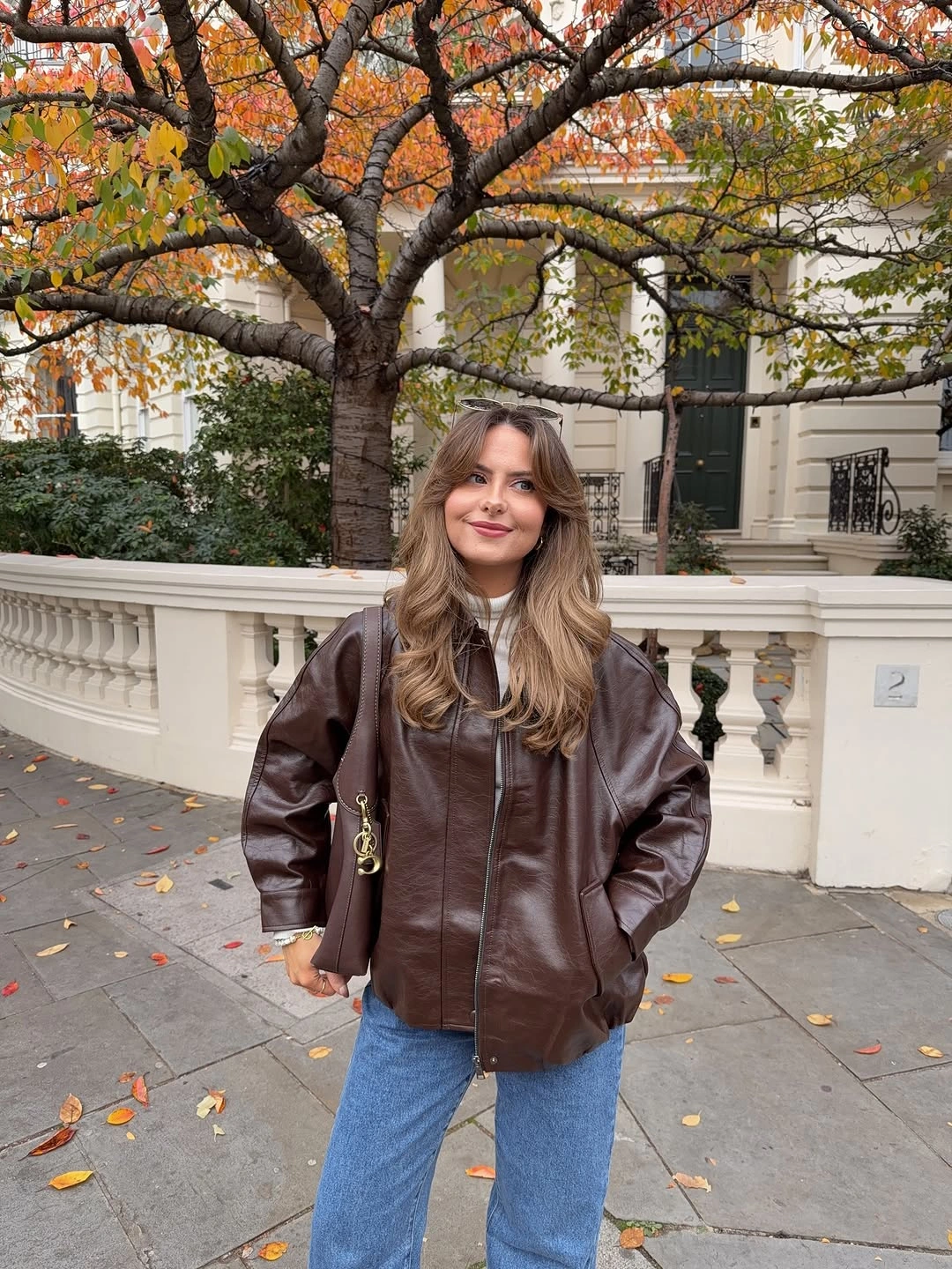 Dark brown moto-style jacket with blue jeans and narrow crossbody strap