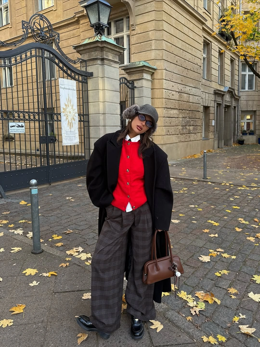 Black jacket over red layer with gray checked trousers and dark hat