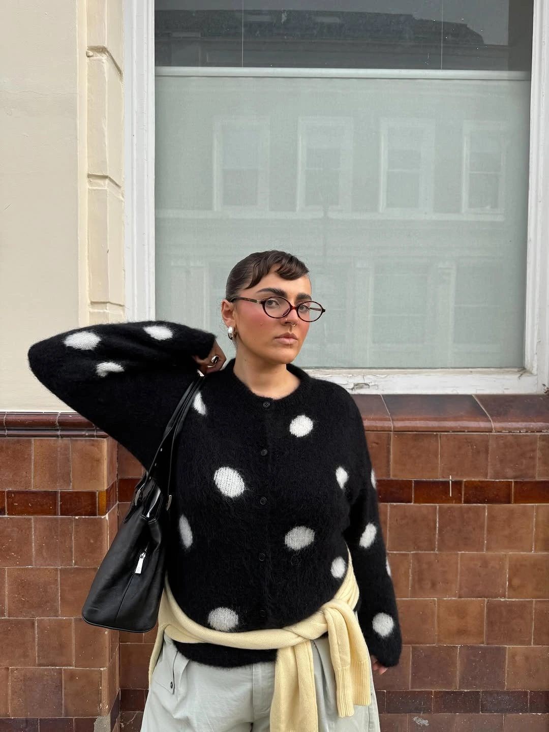 Black spotted sweater with pale yellow shirt tied at waist and black bag