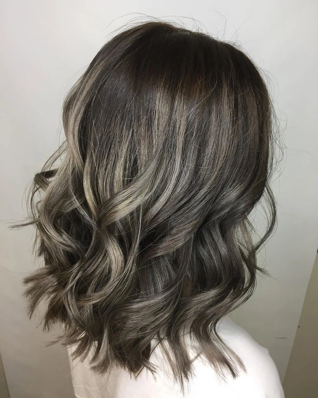 Smoky gray-beige shoulder-length wavy lob with dark root and tousled ends