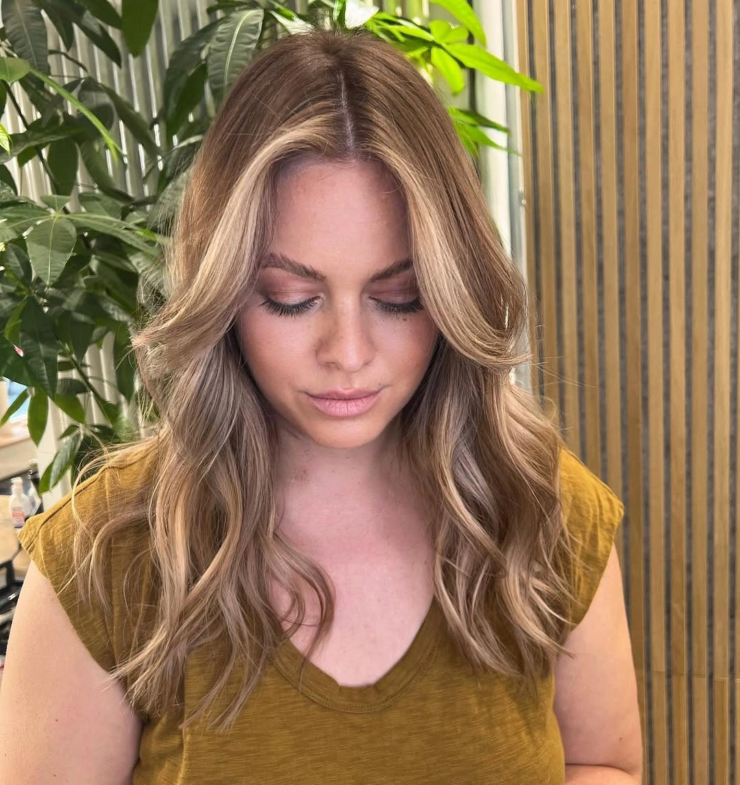 Medium brown wavy hair with warm golden face-framing pieces and center part