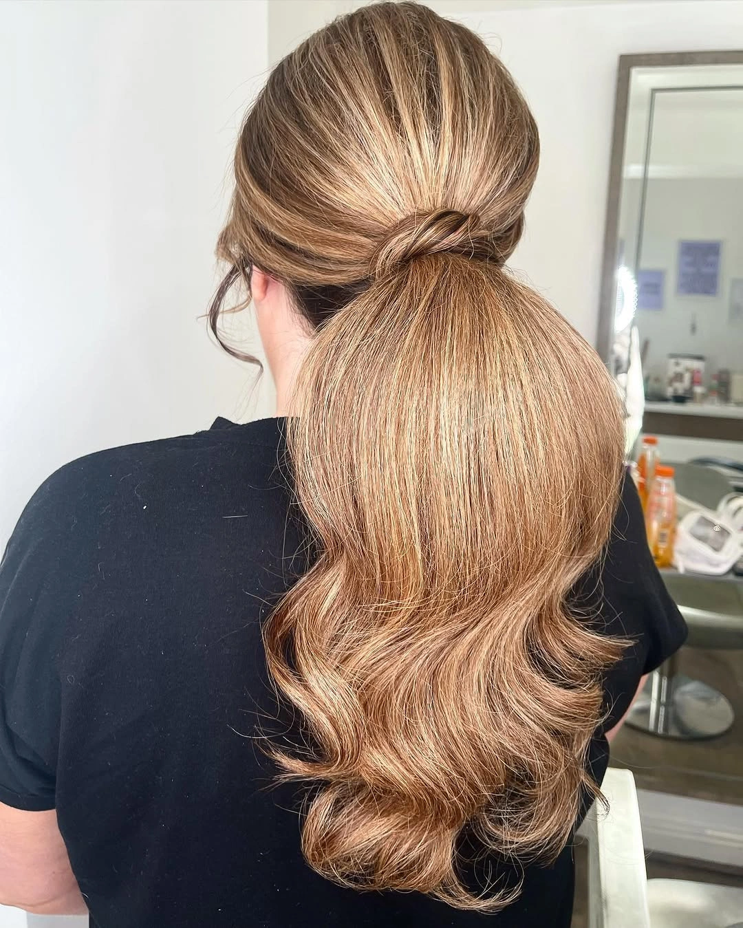 Honey blonde low ponytail with smooth crown, soft root depth, and curled tail