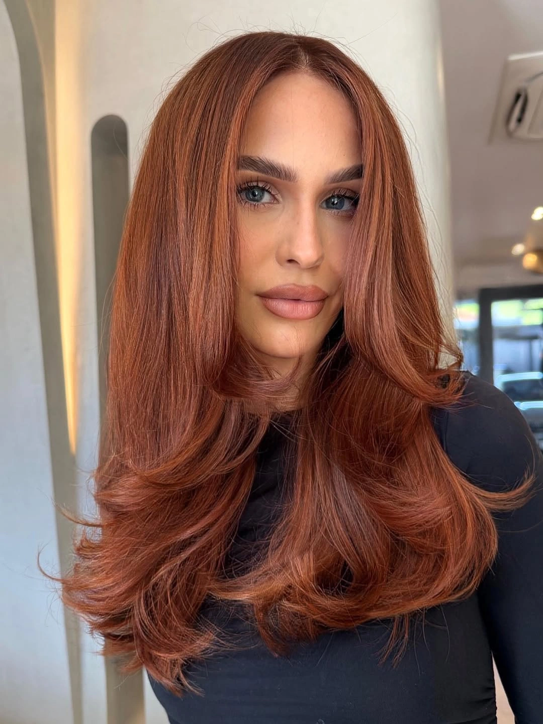 Long copper-brown layered haircut with center part, rounded face frame, and curled ends