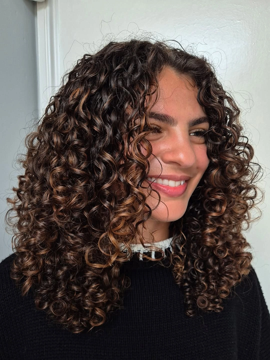 Dark shoulder-length curly haircut with center part and rounded ringlet silhouette