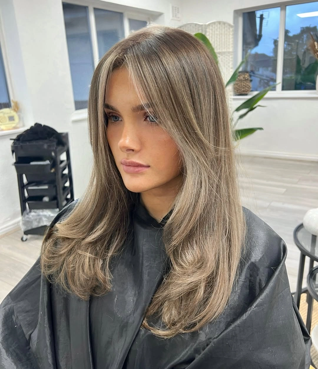 Medium ash-brown layered haircut with long curtain fringe and soft beige ribbons