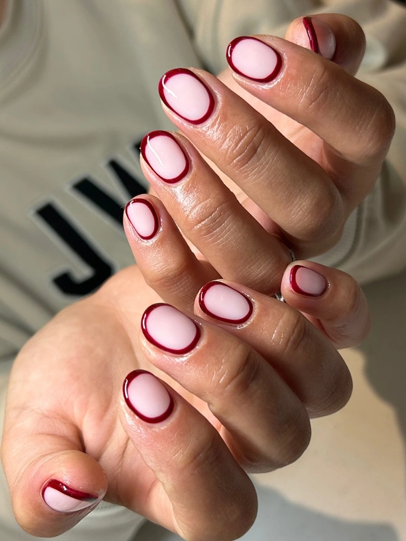 Short pale pink nails with thin burgundy outlines around the edges