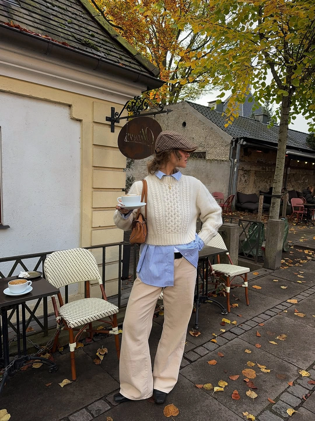 Cream cable sweater over blue striped shirt with beige trousers