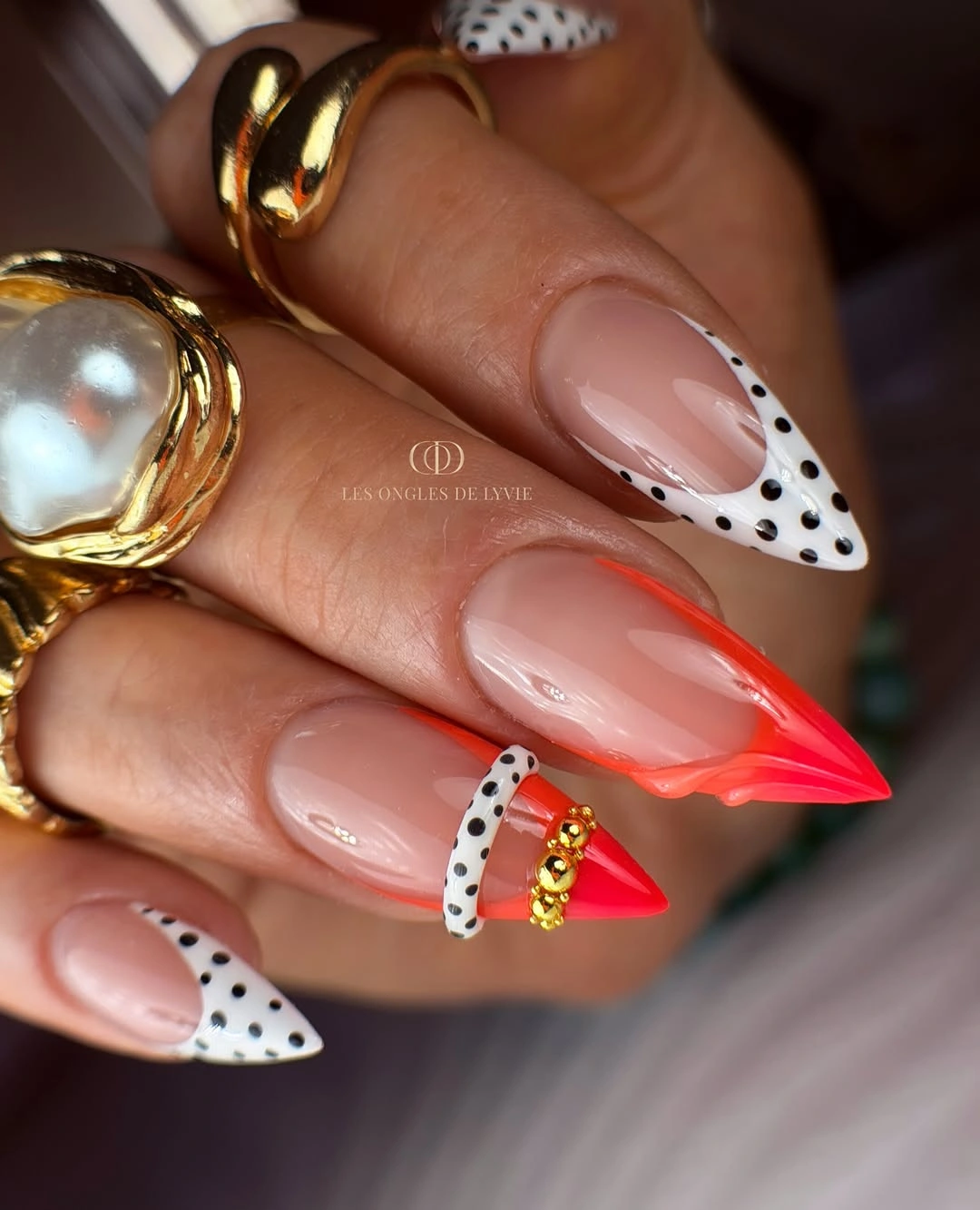 Nude almond nails with black dotted white tips and coral accent