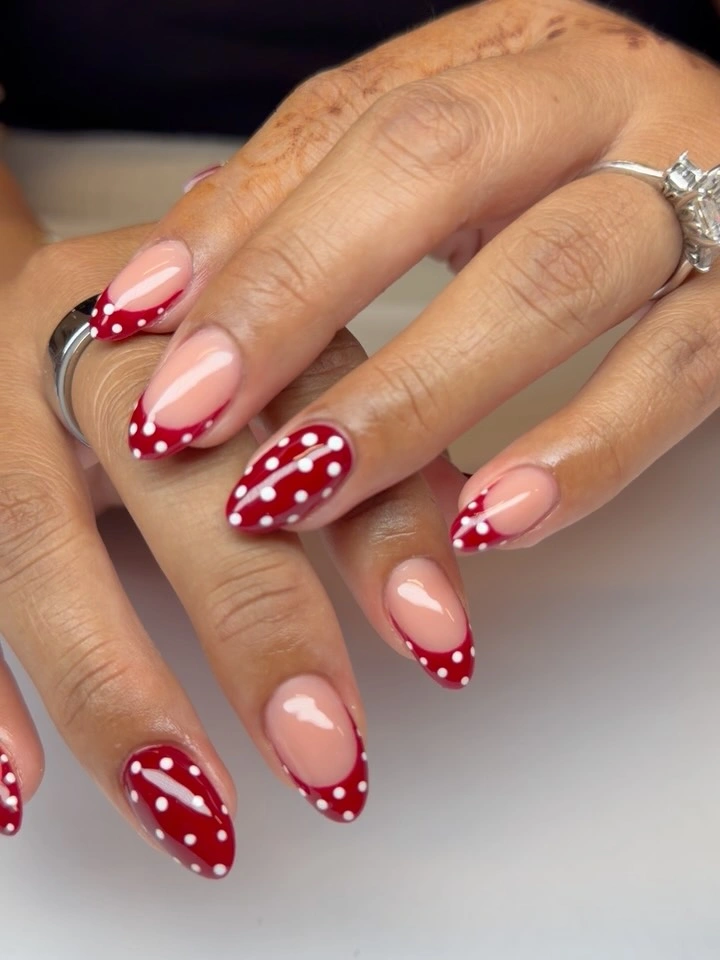 Nude almond nails with pointed red tips and tiny white dots